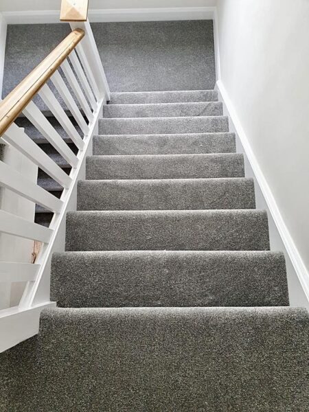 Top view of a grey carpeted staircase with a wooden handrail